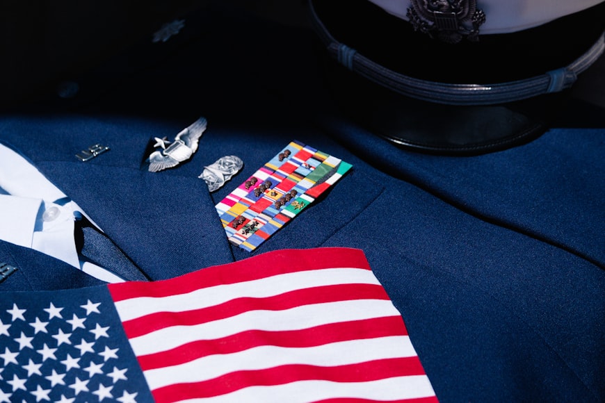A close-up image of an American flag and an official hat lying on top of the suit of a decorated military dress uniform.