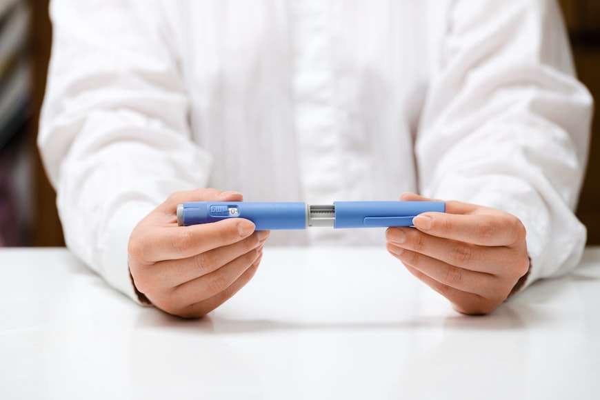 Someone wearing a white shirt holds a tirzepatide injection in both of their hands while resting their arms on a white table.