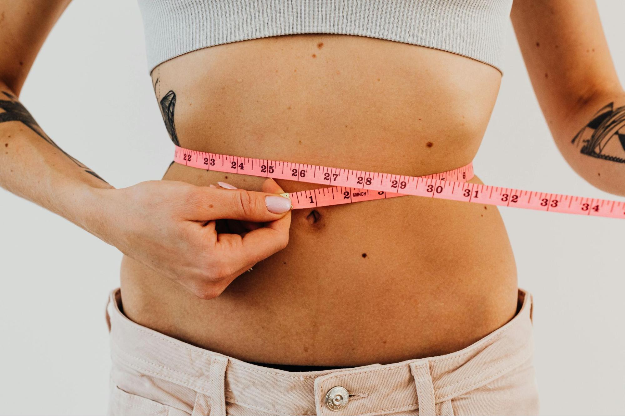 a woman taking her waist measurement with a pink tape measure.