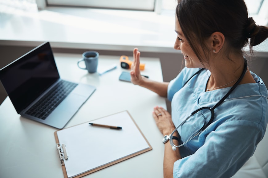 A licensed healthcare provider sits at their desk and conducts a telehealth visit with a patient on their laptop.