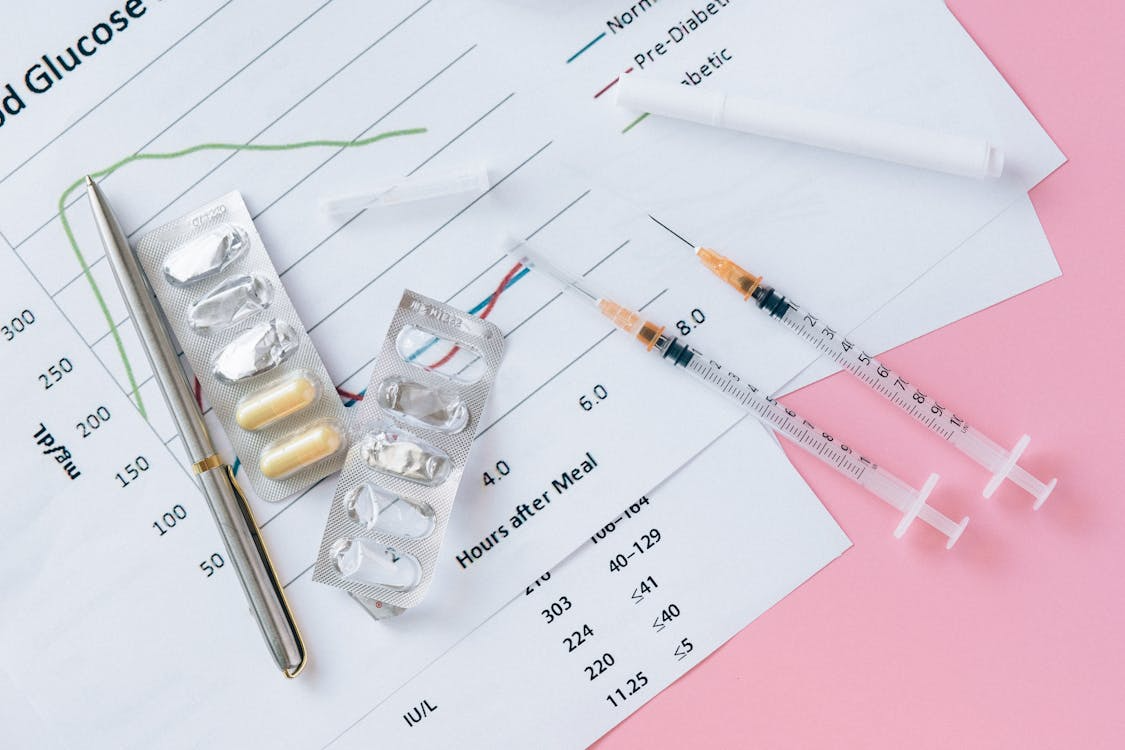 Syringes, tablets and a pen on diabetes and glucose paperwork