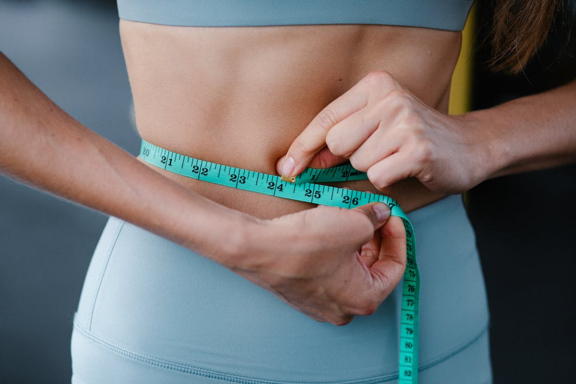 Woman wearing blue activewear wrapping a measuring tape around her waist