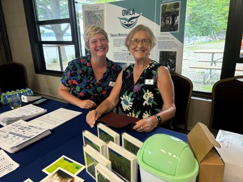 Two women sitting at a table with a green container in front of them.