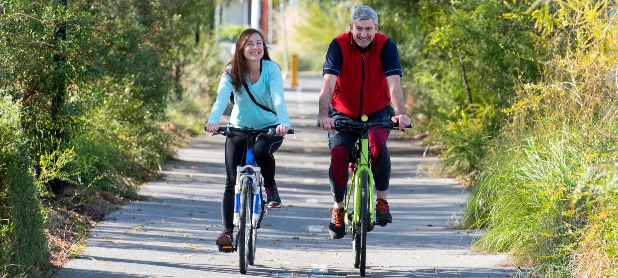 man and woman cycling through a tree tunnel on a cycle path