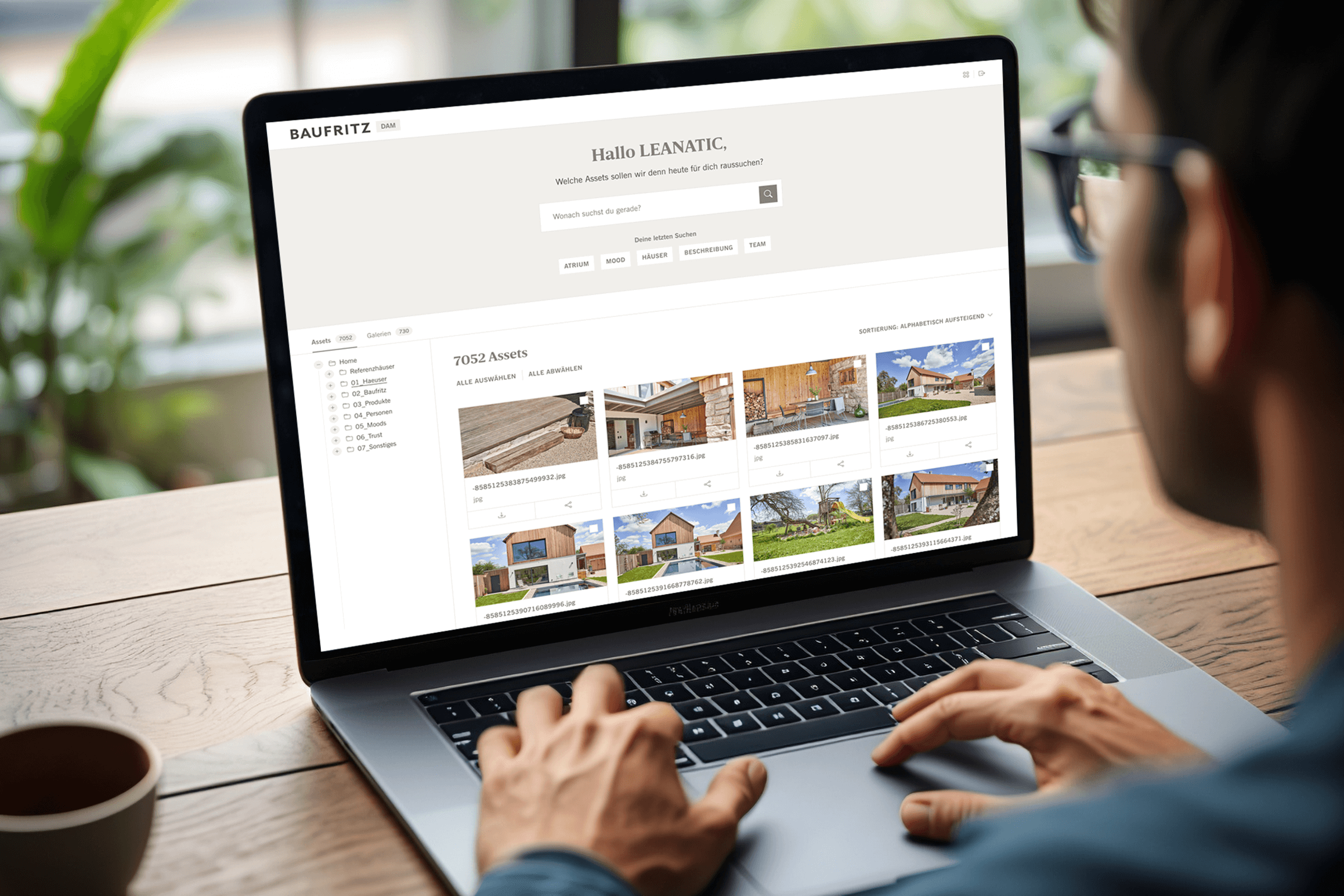 Ein Mann mit Brille arbeitet an einem geöffneten Laptop. Man sieht über seine Schulter auf den Bildschirm. Der Bildschirm zeigt die Übersicht des Digital Asset Management Systems.