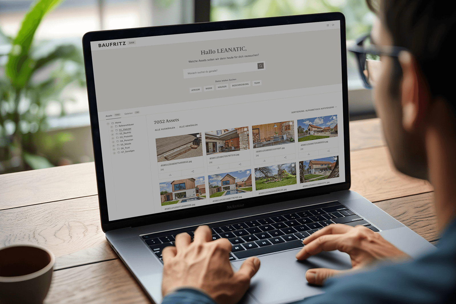 Ein Mann mit Brille arbeitet an einem geöffneten Laptop. Man sieht über seine Schulter auf den Bildschirm. Der Bildschirm zeigt die Übersicht des Digital Asset Management Systems.