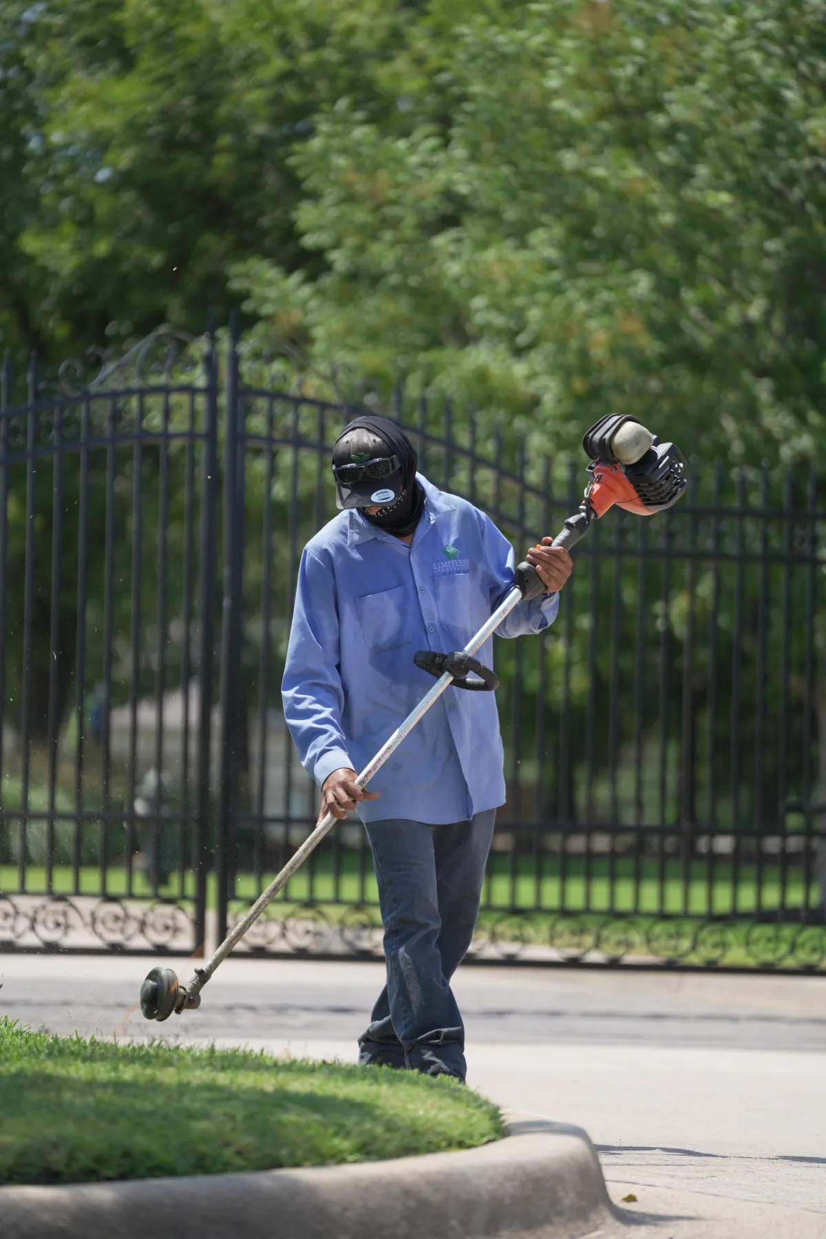 Landscaping crew member trimming grass beside a metal fence