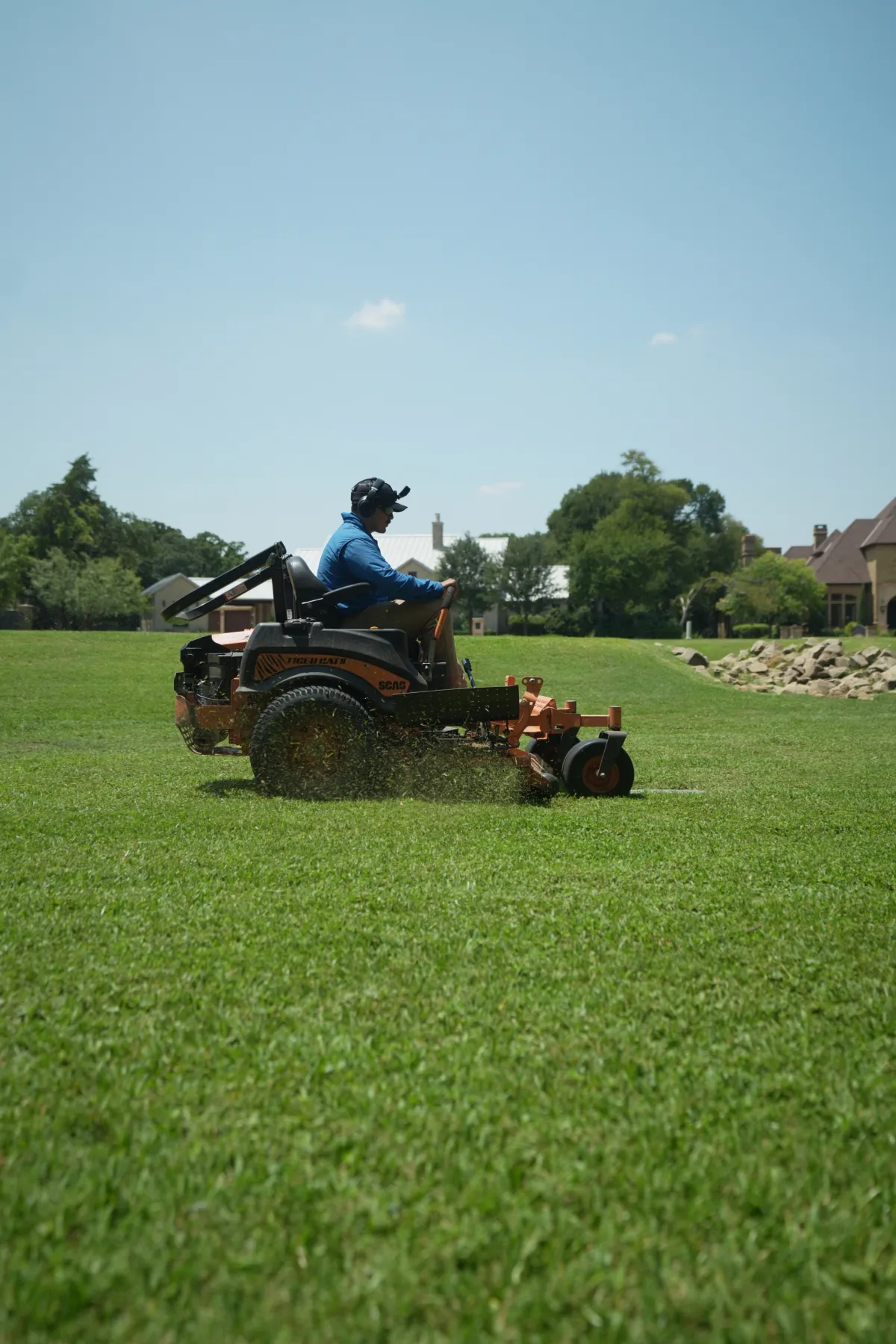 Landscaping crew member mowing a large lawn with a zero-turn mower