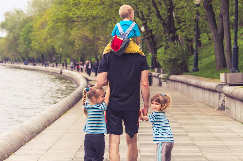 A father walking with this three kids along a lake