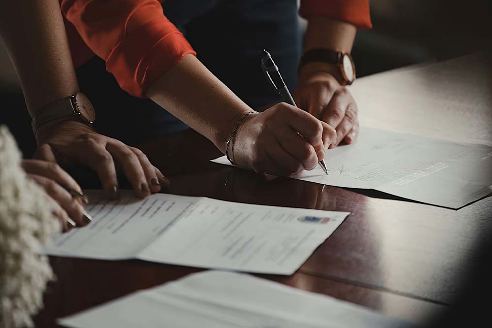Close up of two people signing paperwork on a dark oak table