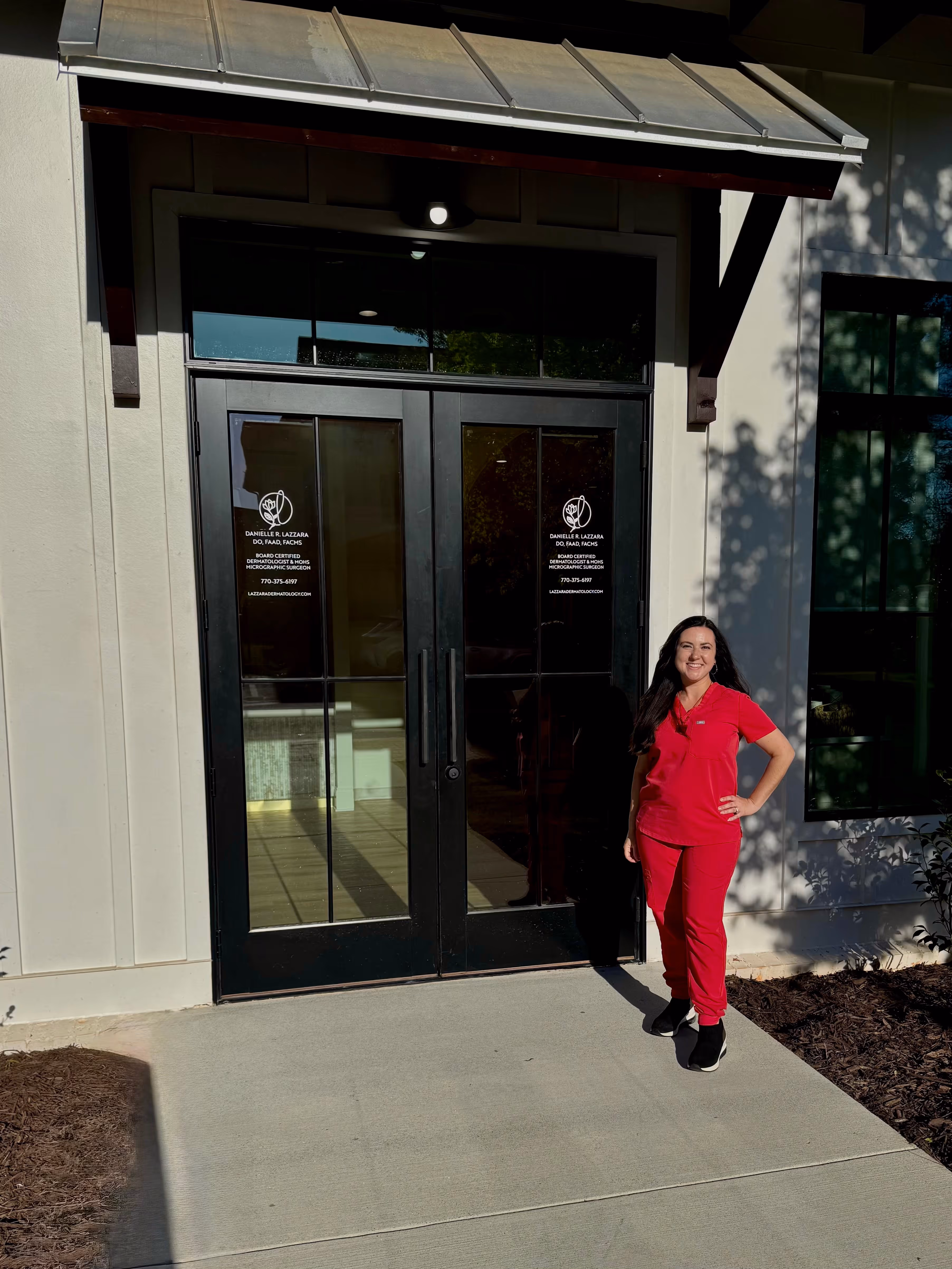 A woman in a red jumpsuit standing in front of a building.