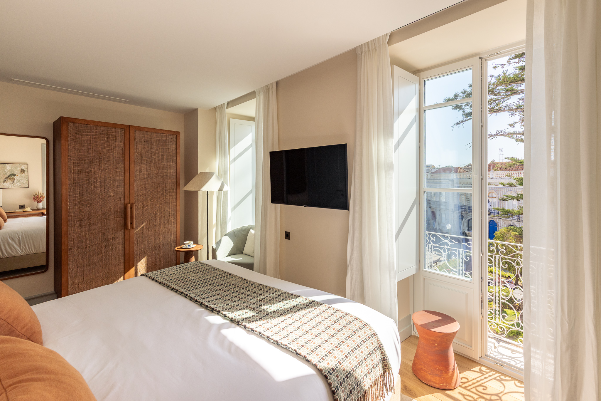 Bright and elegant hotel room with a double bed featuring gray pillows, a patterned bedspread, and a vase of flowers on the bedside table beside a sheer curtain filtering natural light - Palacio de Tavira