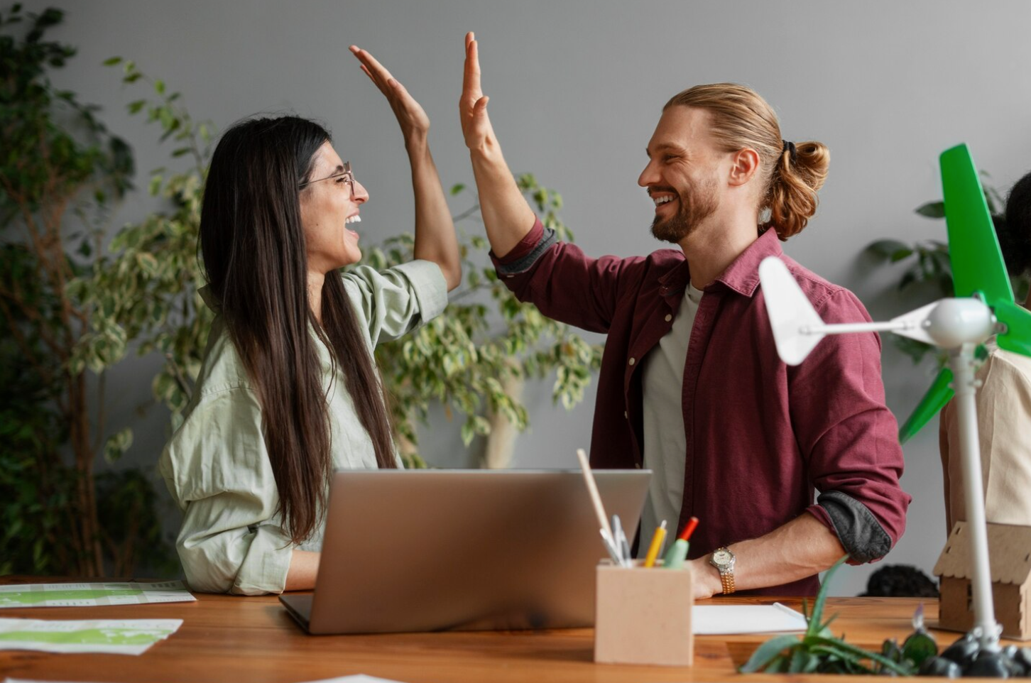 Two people high-fiving at a desk with a laptop, celebrating the successful completion of an alcohol rehab program