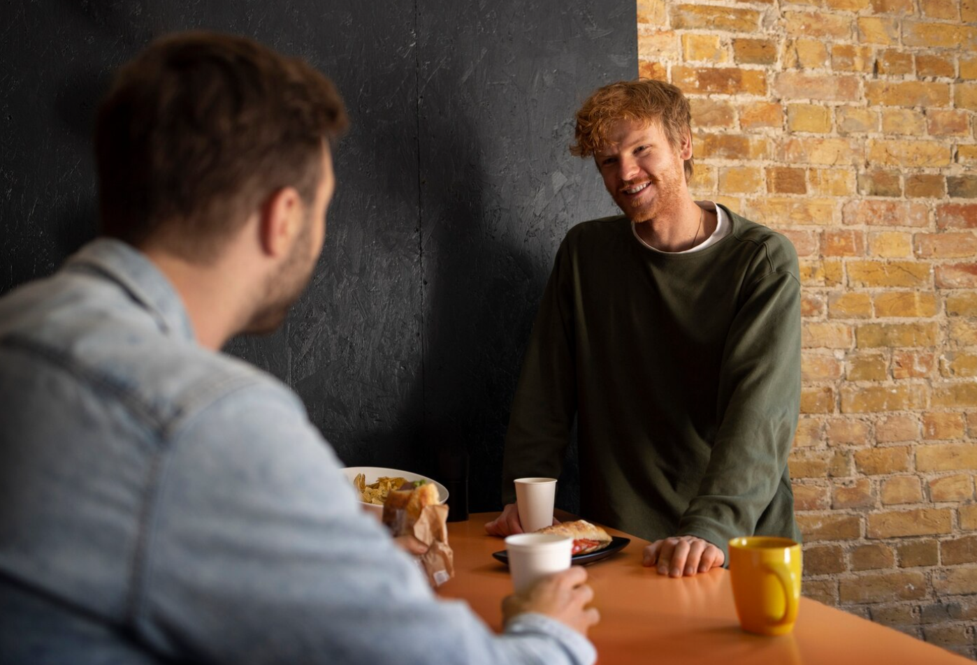 Two men talk at a café table, one listening attentively, symbolizing supportive conversations during addiction recovery