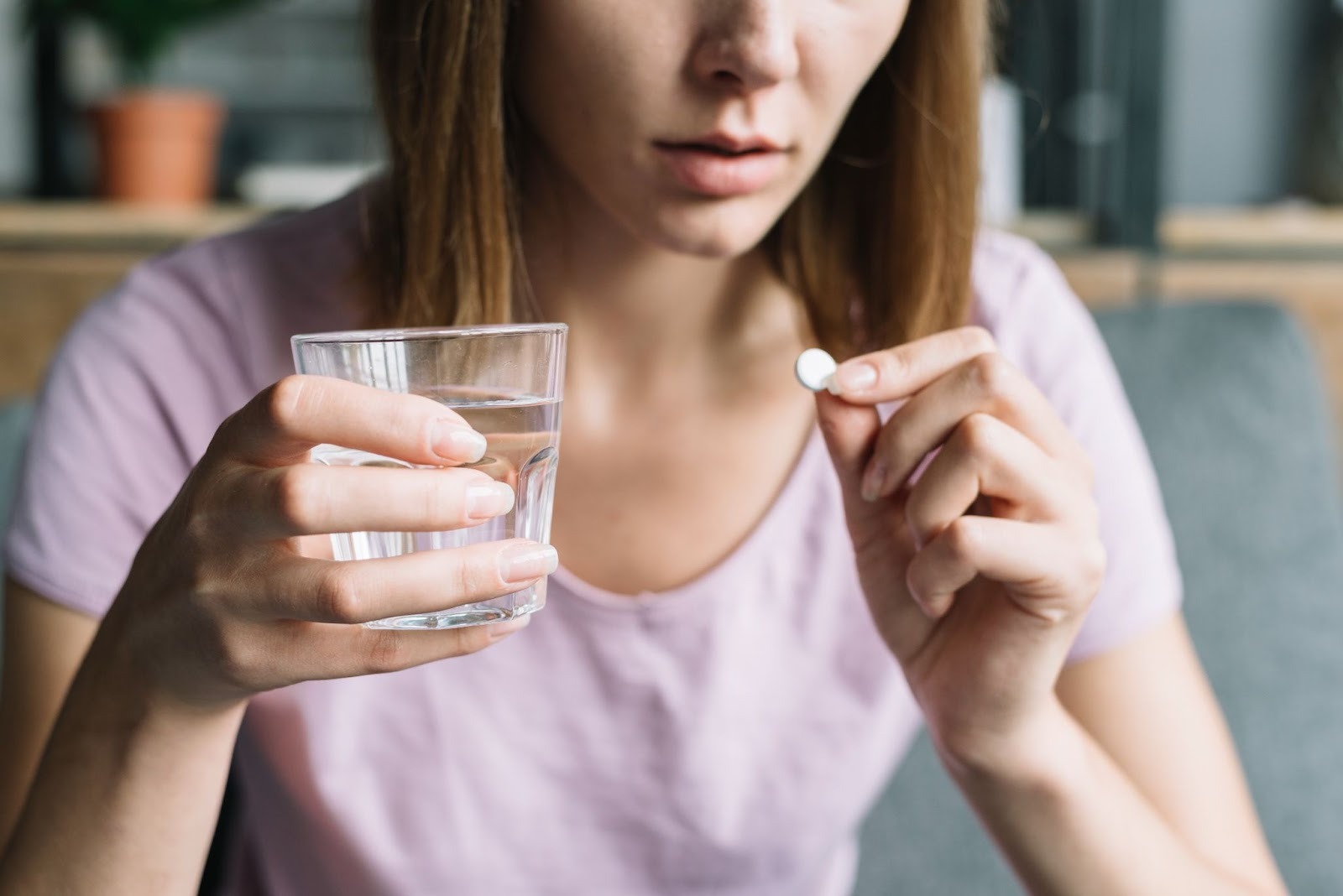 A woman holding a pill and glass of water, depicting she could be addicted to prescription drugs