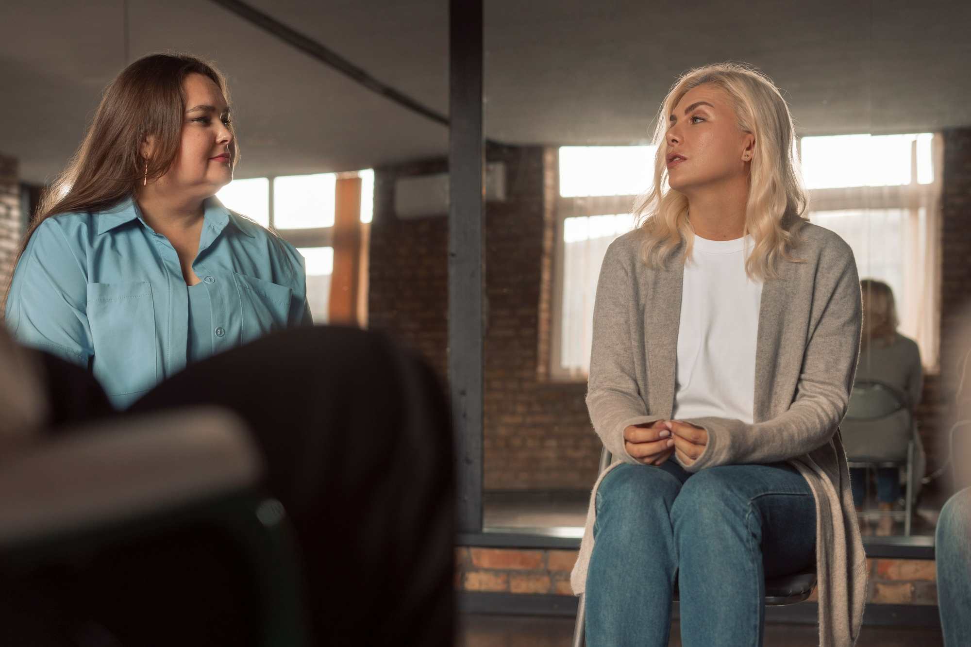 Two women participating in a supportive group therapy session for addiction recovery in a welcoming counseling environment.