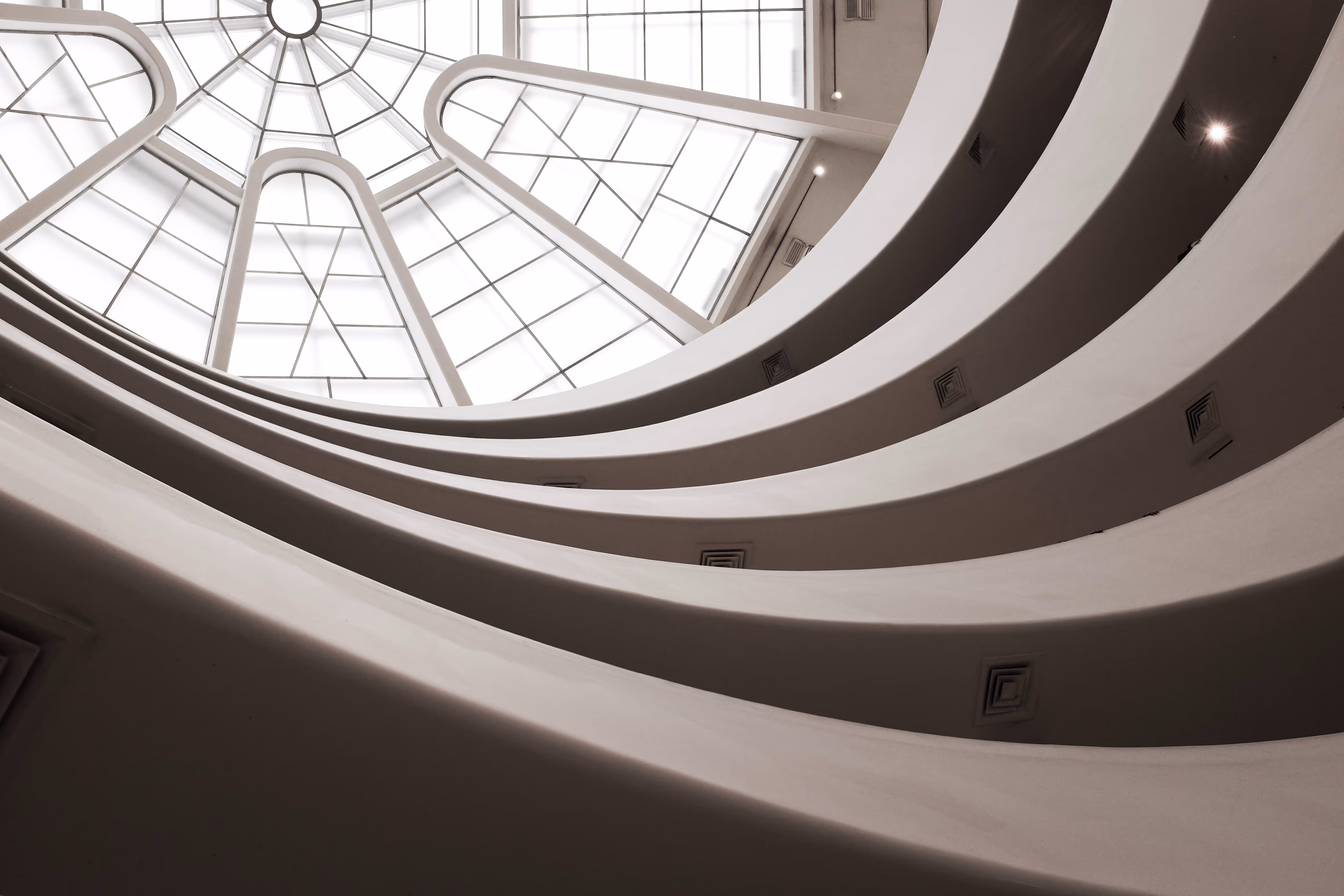 Interior view looking up at curved balconies and geometric glass ceiling of a modern building.