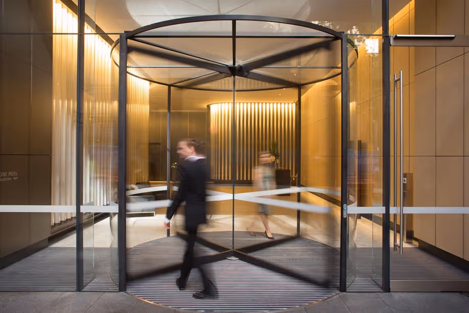 Blurred motion of a man in a suit and a woman walking through a revolving glass door entrance with warm interior lighting.