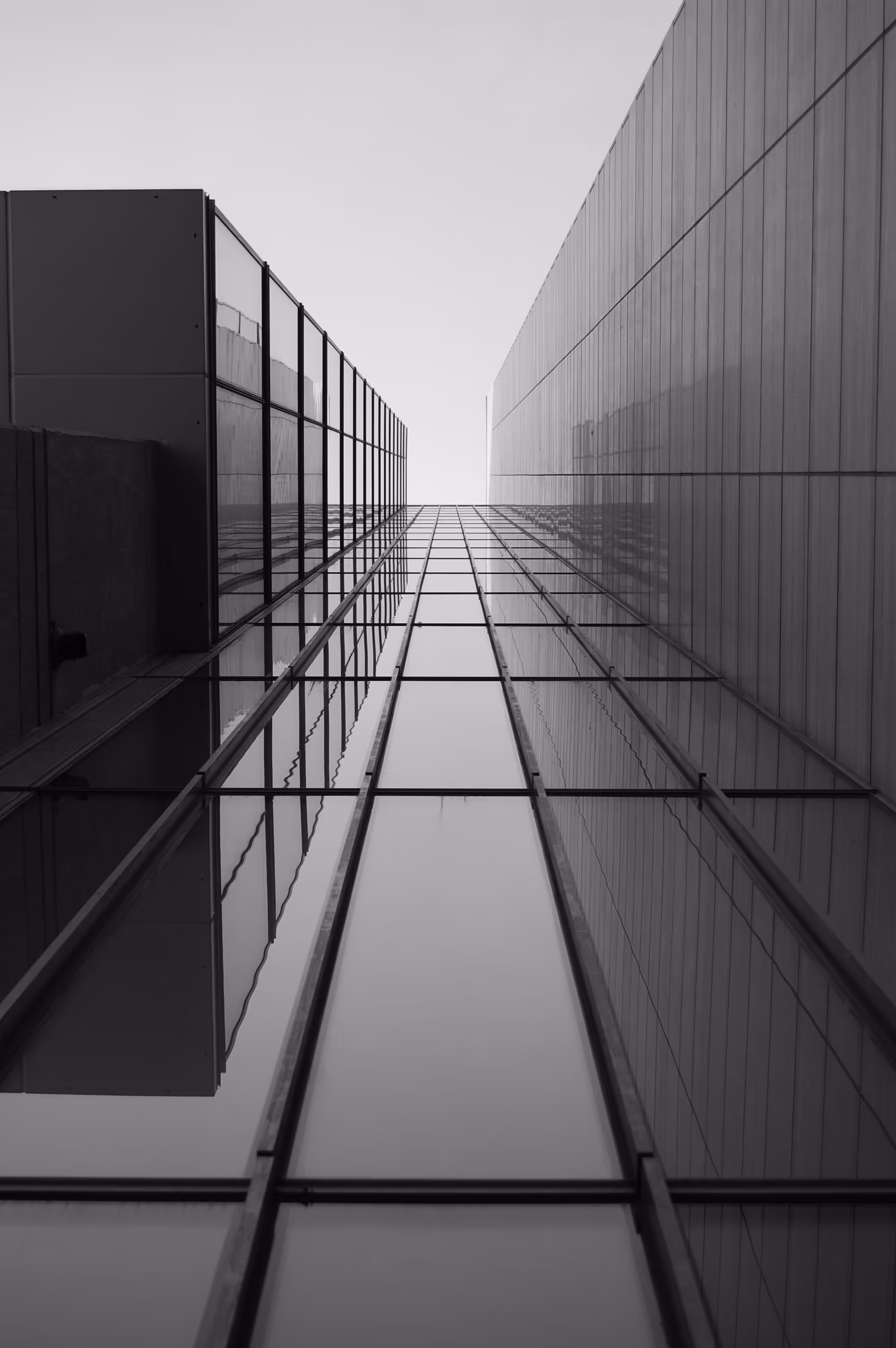 Black and white vertical view looking up between two tall glass buildings.
