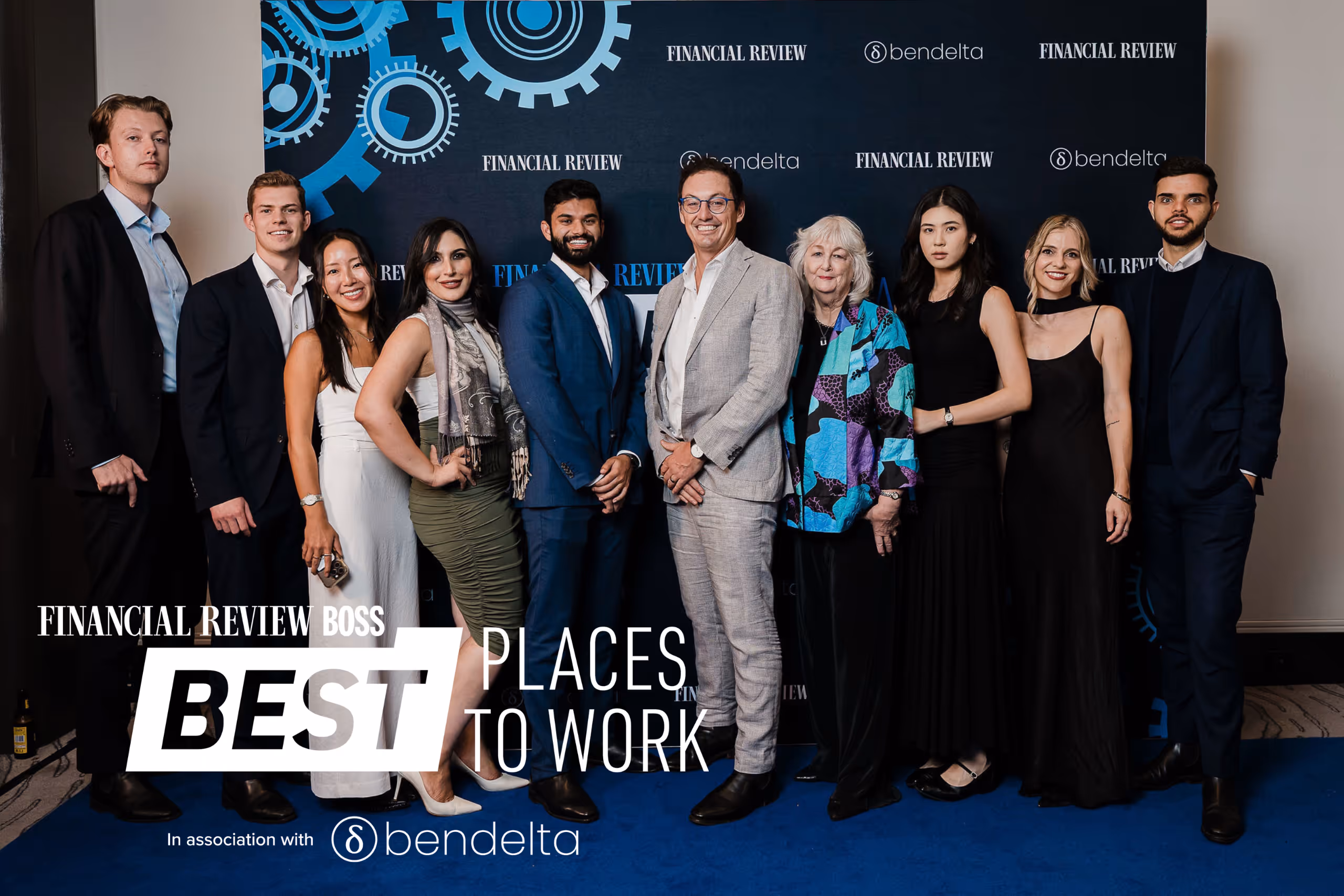 Group of professionally dressed people standing on a blue carpet in front of a backdrop with Financial Review and Bendelta logos, text reads 'Financial Review Boss Best Places to Work'.