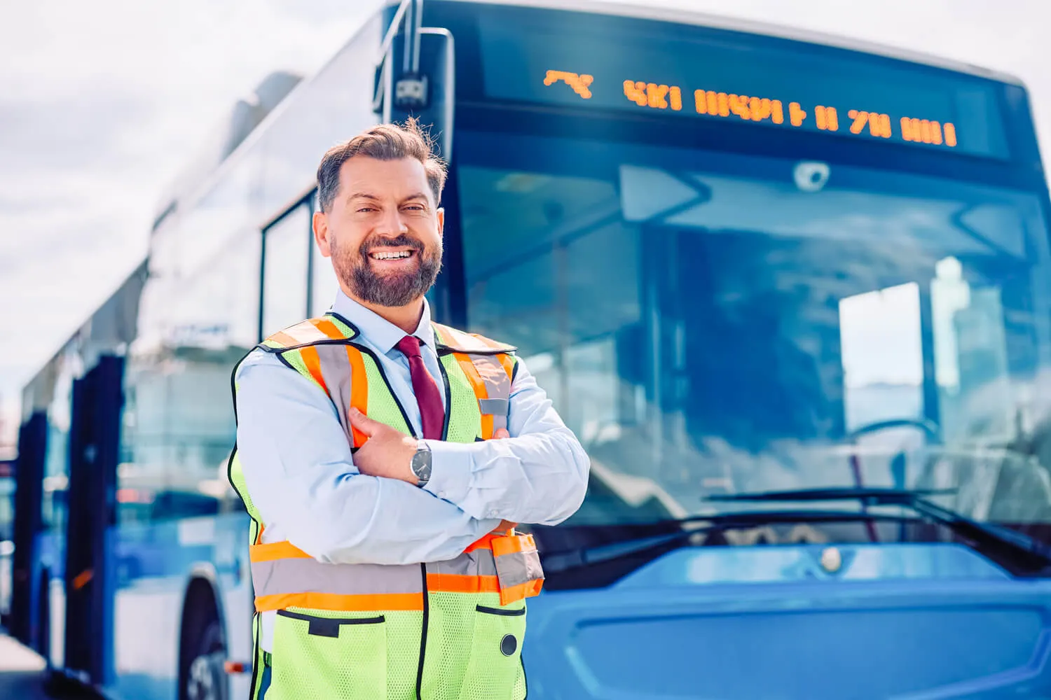 Confident transport manager standing in front of city bus wearing safety vest