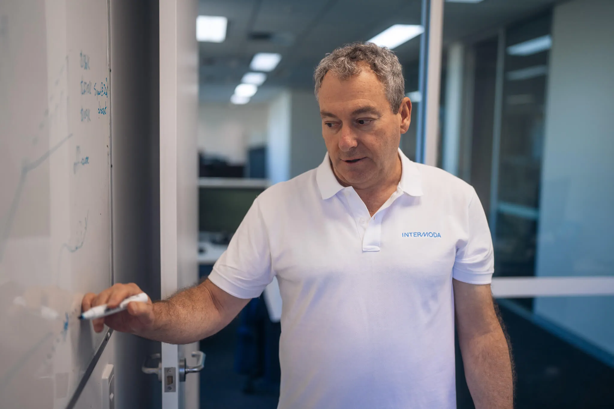 Team member in Intermoda polo shirt writing on a whiteboard during a planning session