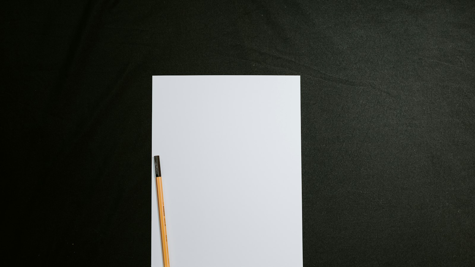 Feuille de papier blanche et vierge posée sur un tissu noir au grain visible, cadrage épuré en lumière douce