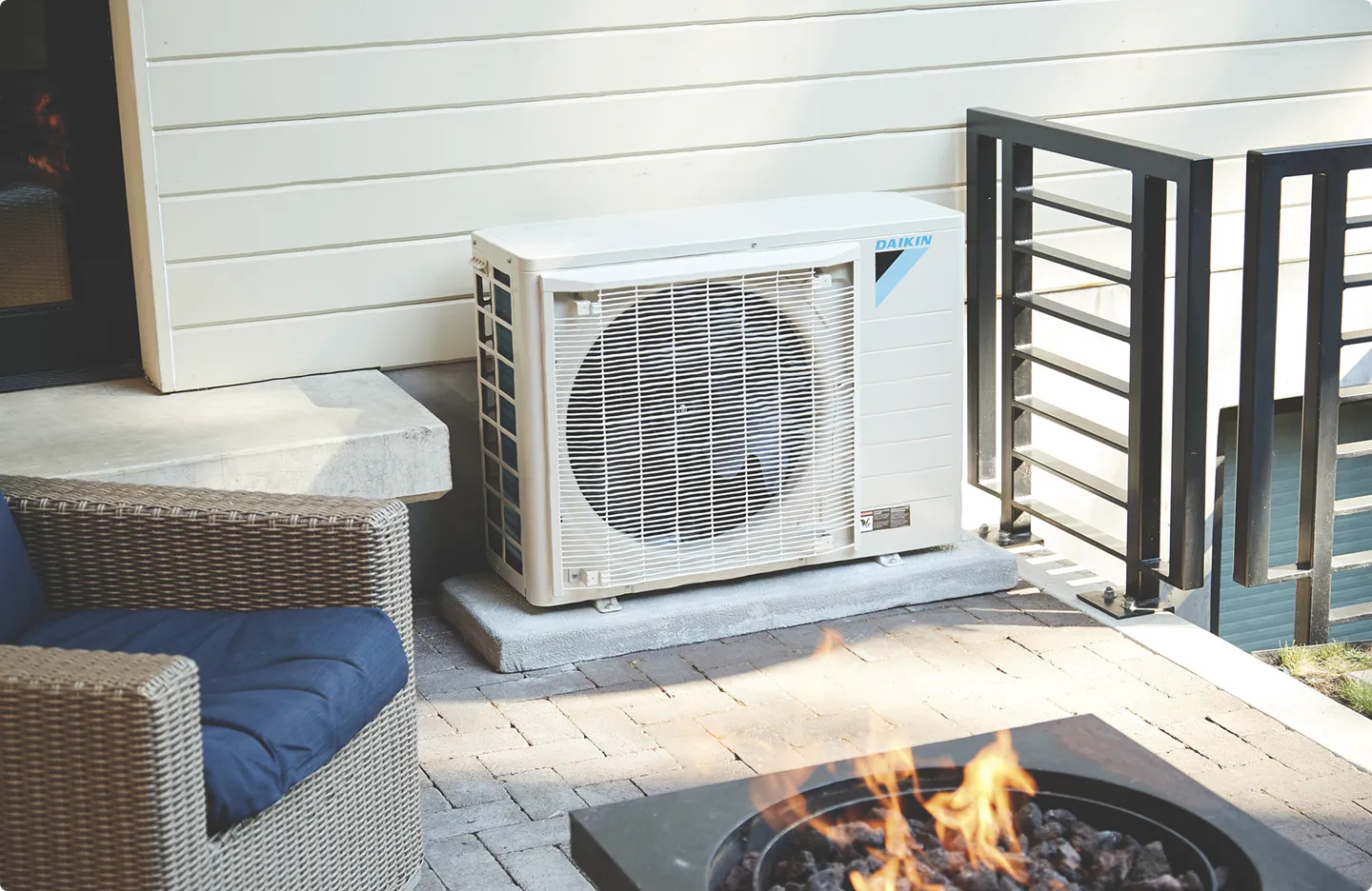 Daikin air conditioner outdoor unit on patio with fire pit and wicker furniture