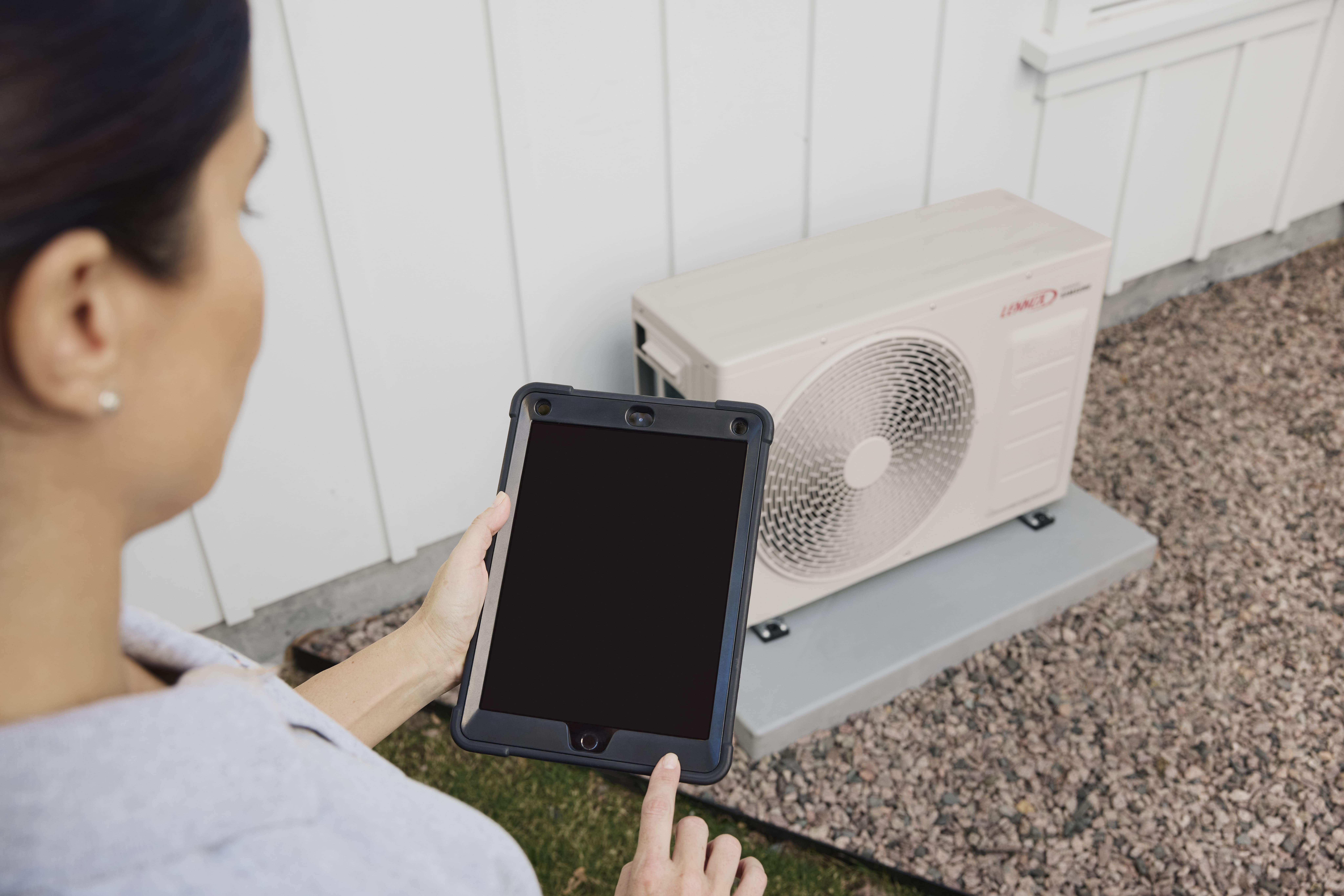 Female technician standing above HVAC heat pump unit.