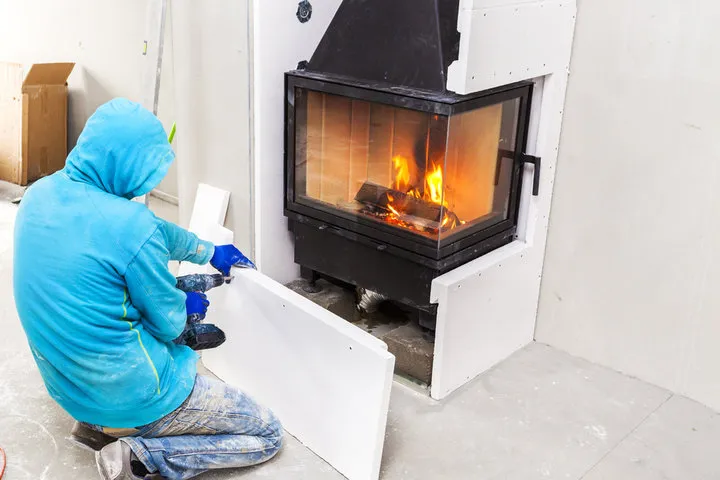 Person in blue hoodie warming up near modern corner fireplace