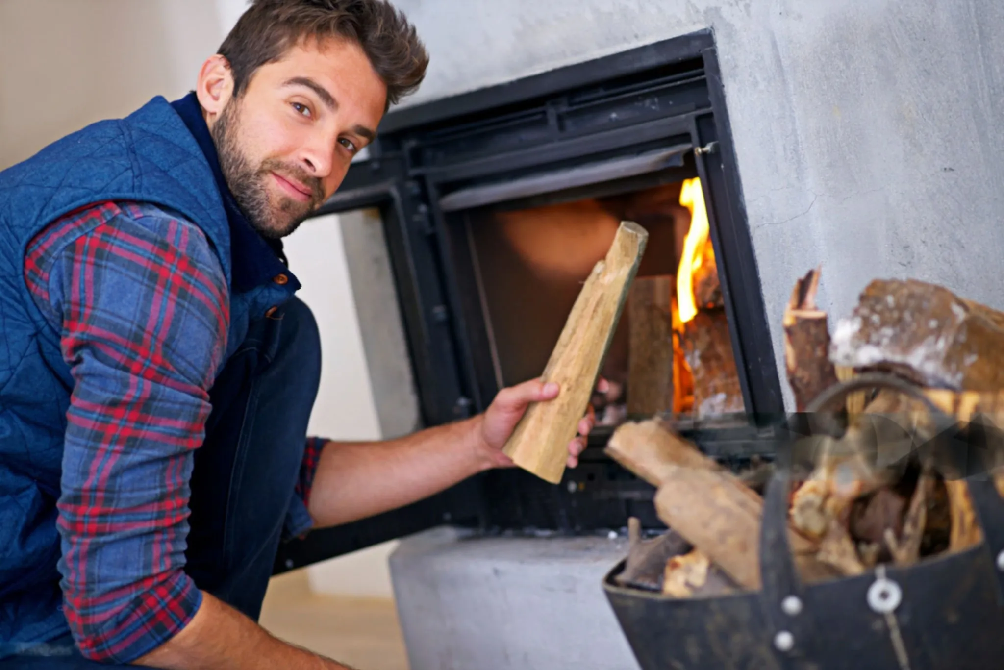 Man in plaid shirt adding wood to a burning fireplace