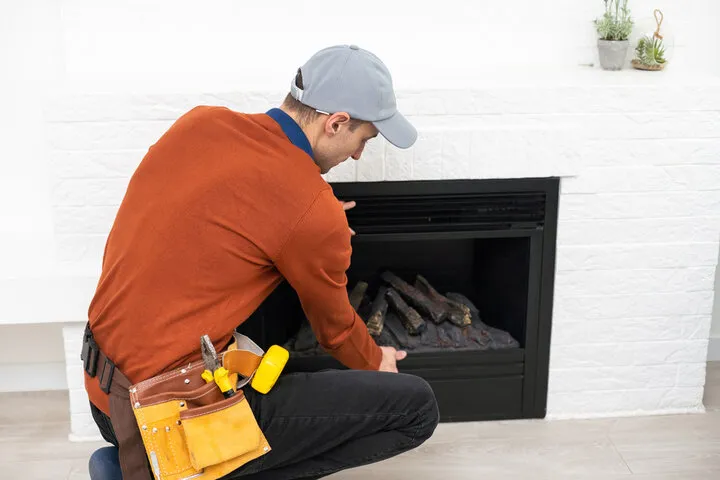 Technician in orange shirt checking fireplace with tool belt