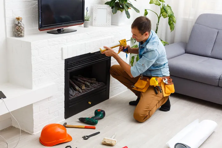Handyman repairing fireplace with tools and safety helmet nearby