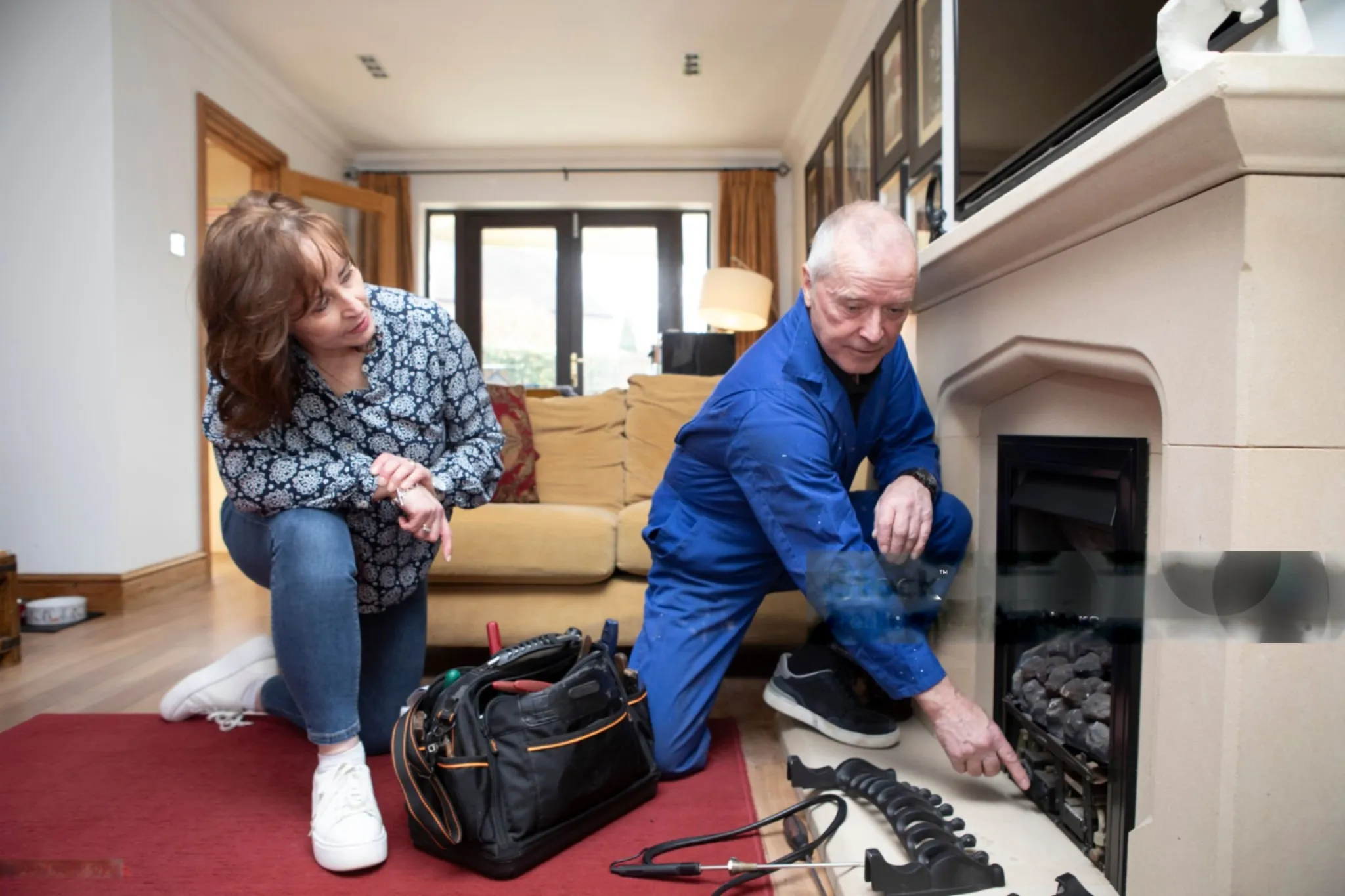 Technician repairing fireplace while homeowner watches in living room