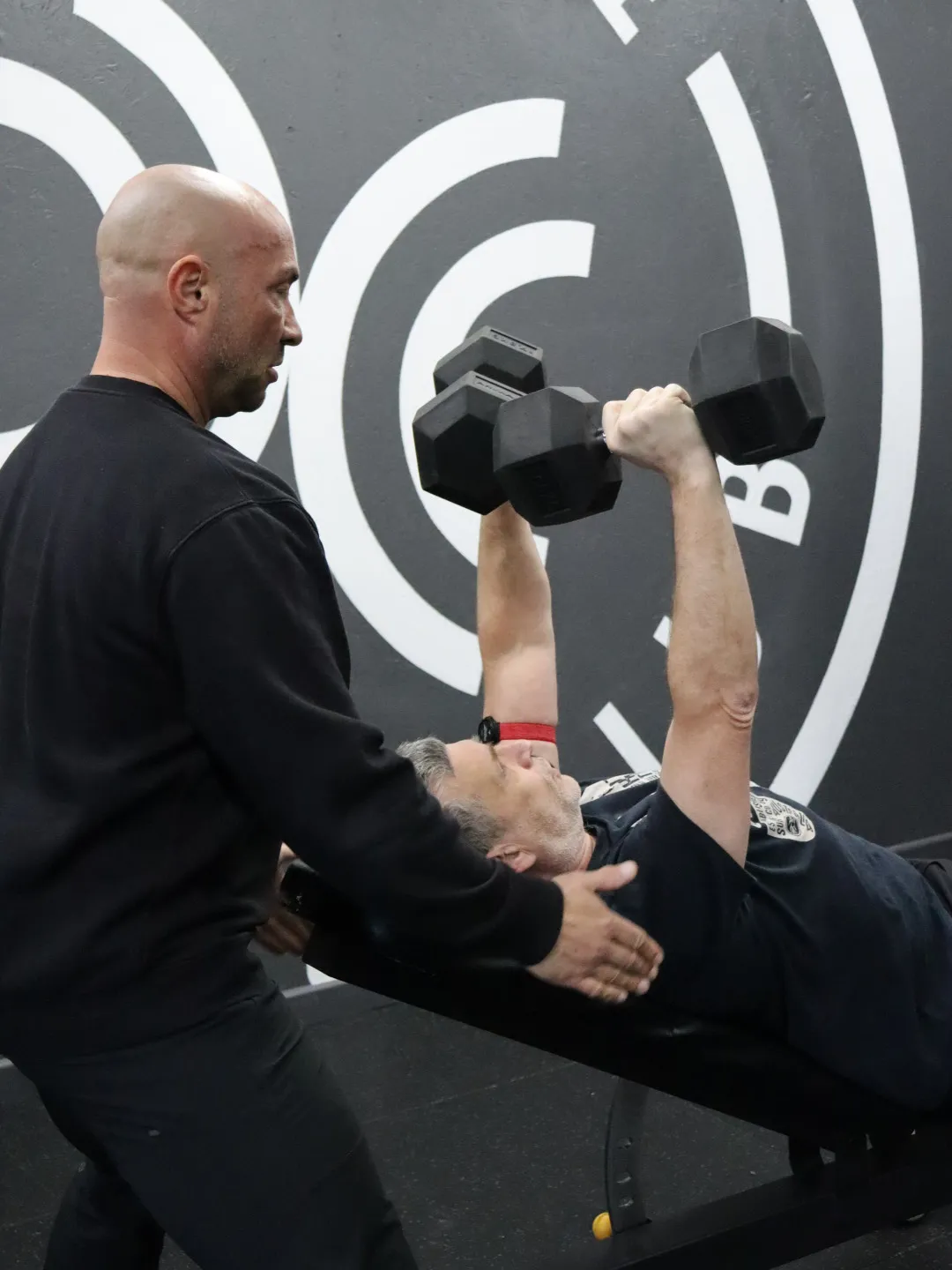 A HUSTLE personal trainer supporting a member doing a chest press