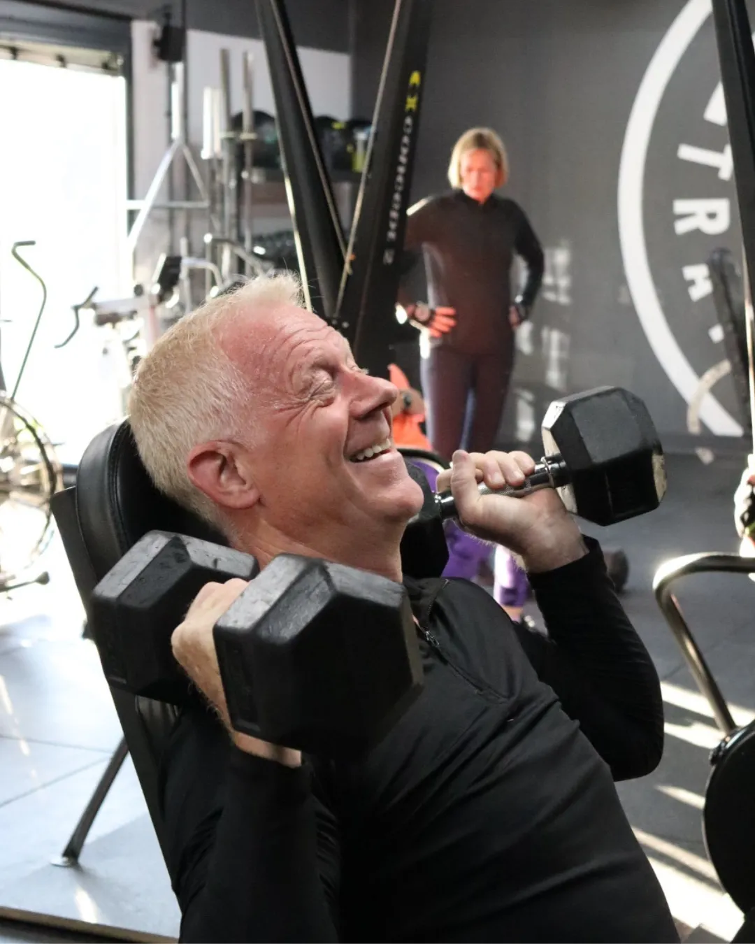 A HUSTLE member doing a shoulder press smiling