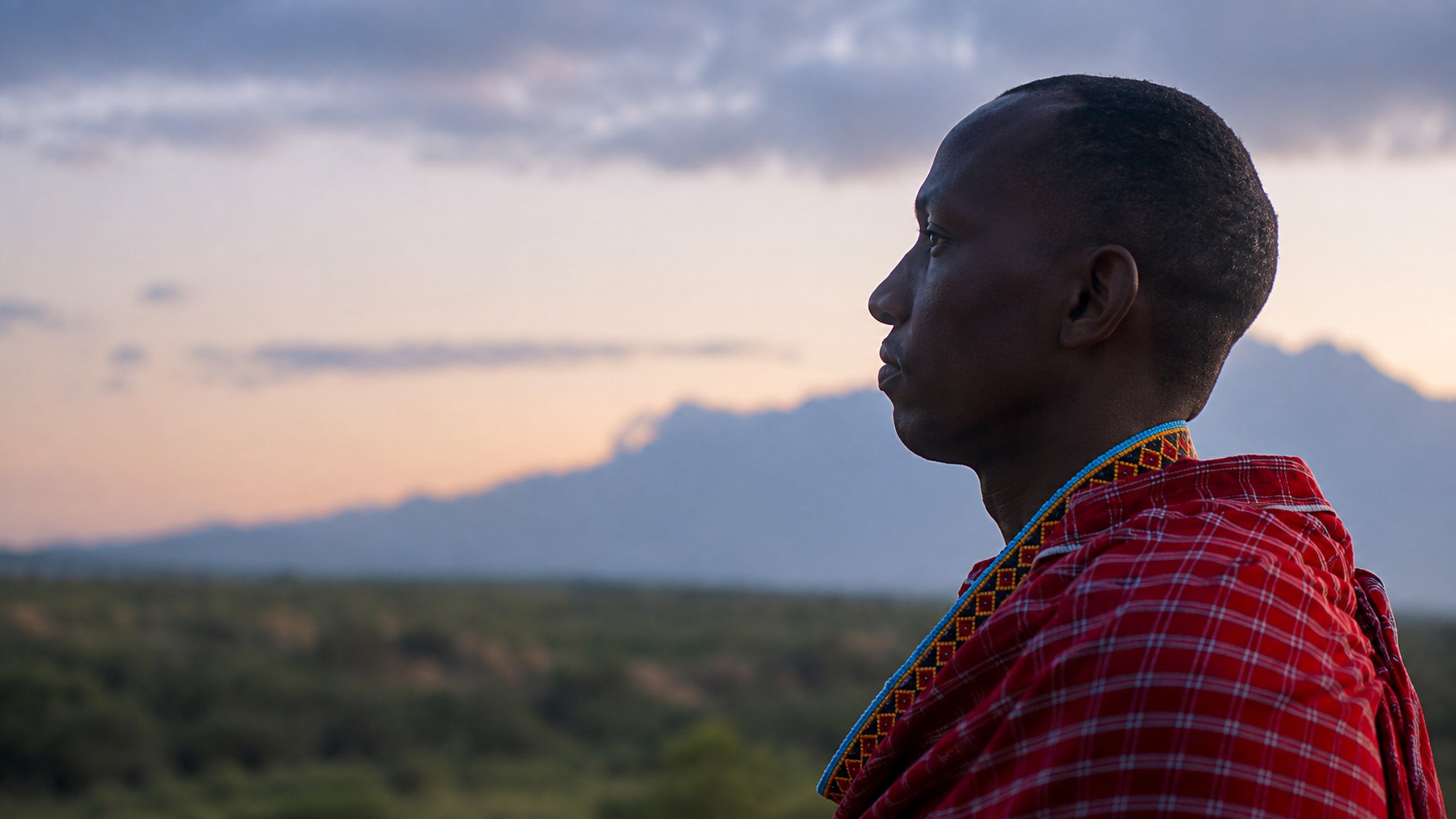 A Maasai man in traditional red clothing standing before Mount Meru