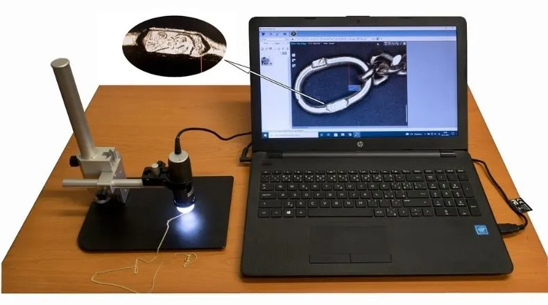 Laptop s obrazem detailu kovového řetězu z lupy ve stojanu na stole.