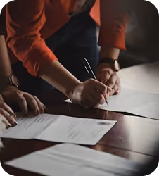 Person signing document at desk with red-sleeved shirt