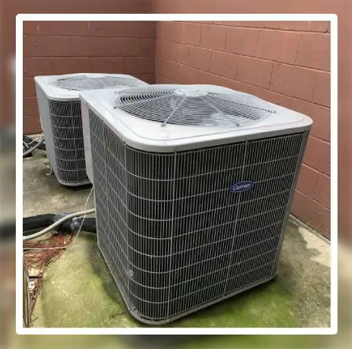 Two outdoor air conditioning units sitting on concrete next to brick wall