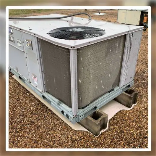 Large industrial HVAC unit sitting on concrete blocks on gravel ground