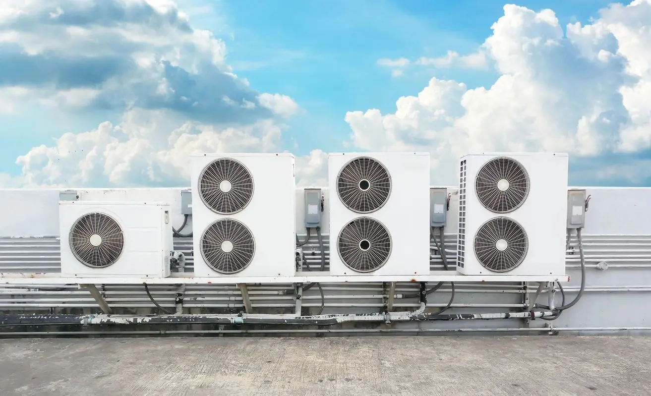 Multiple white air conditioning units on rooftop against cloudy blue sky