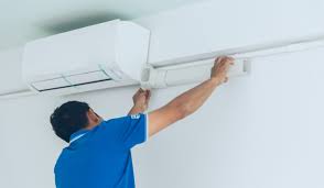 Technician in blue shirt installing or repairing a white air conditioning unit
