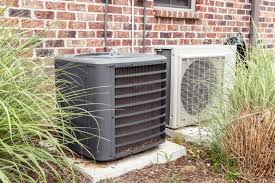 Two outdoor HVAC units next to brick wall and landscaped garden area