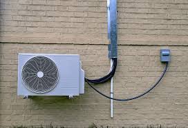 White air conditioning unit mounted on brick wall with electrical conduit