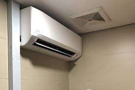 Modern white air conditioning unit mounted on beige wall with vent