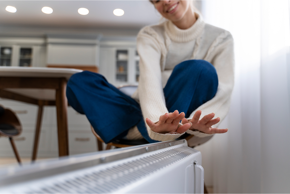 Person in white sweater warming hands on electric heater at home