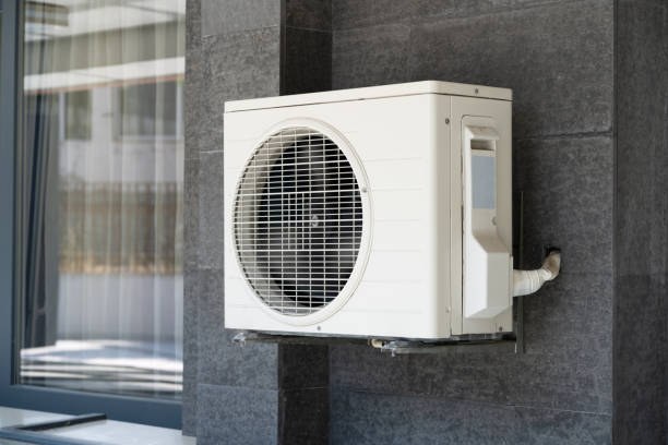 White air conditioning unit mounted on gray exterior wall near window