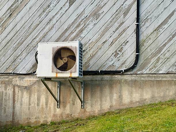 Old air conditioning unit mounted on weathered wooden wall with pipe