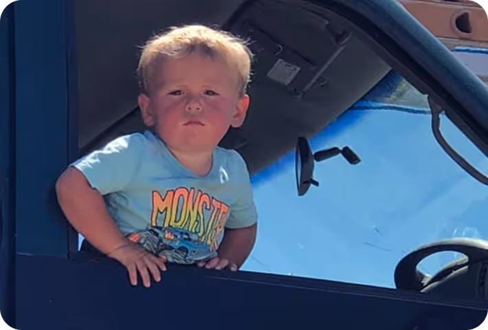 A little boy sitting in the drivers seat of a truck.